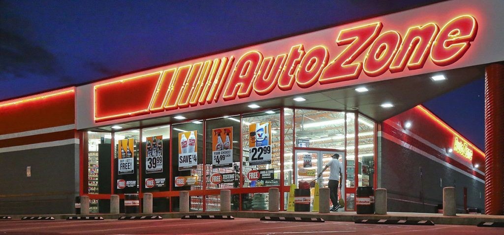 An AutoZone store with posters of products displayed on glass walls and logo on top written with neon lights