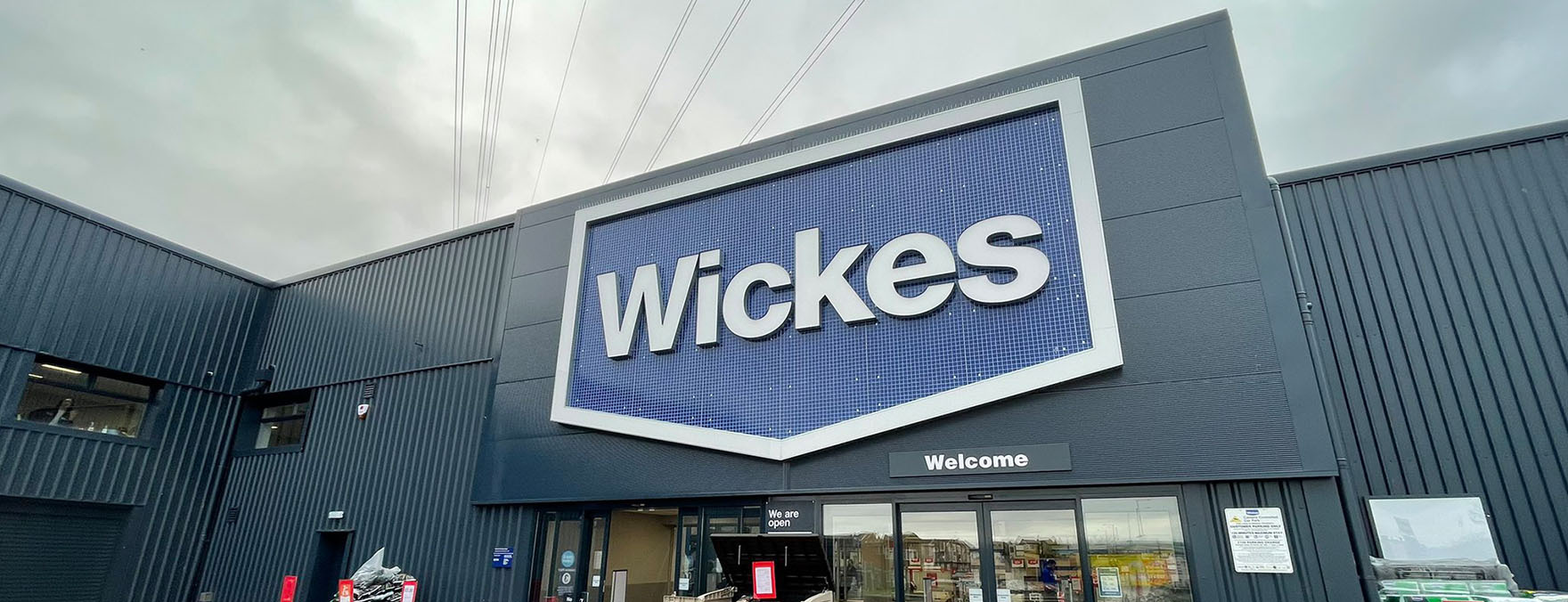 The Wickes Group Plc logo is painted in blue and white on the storefront wall.