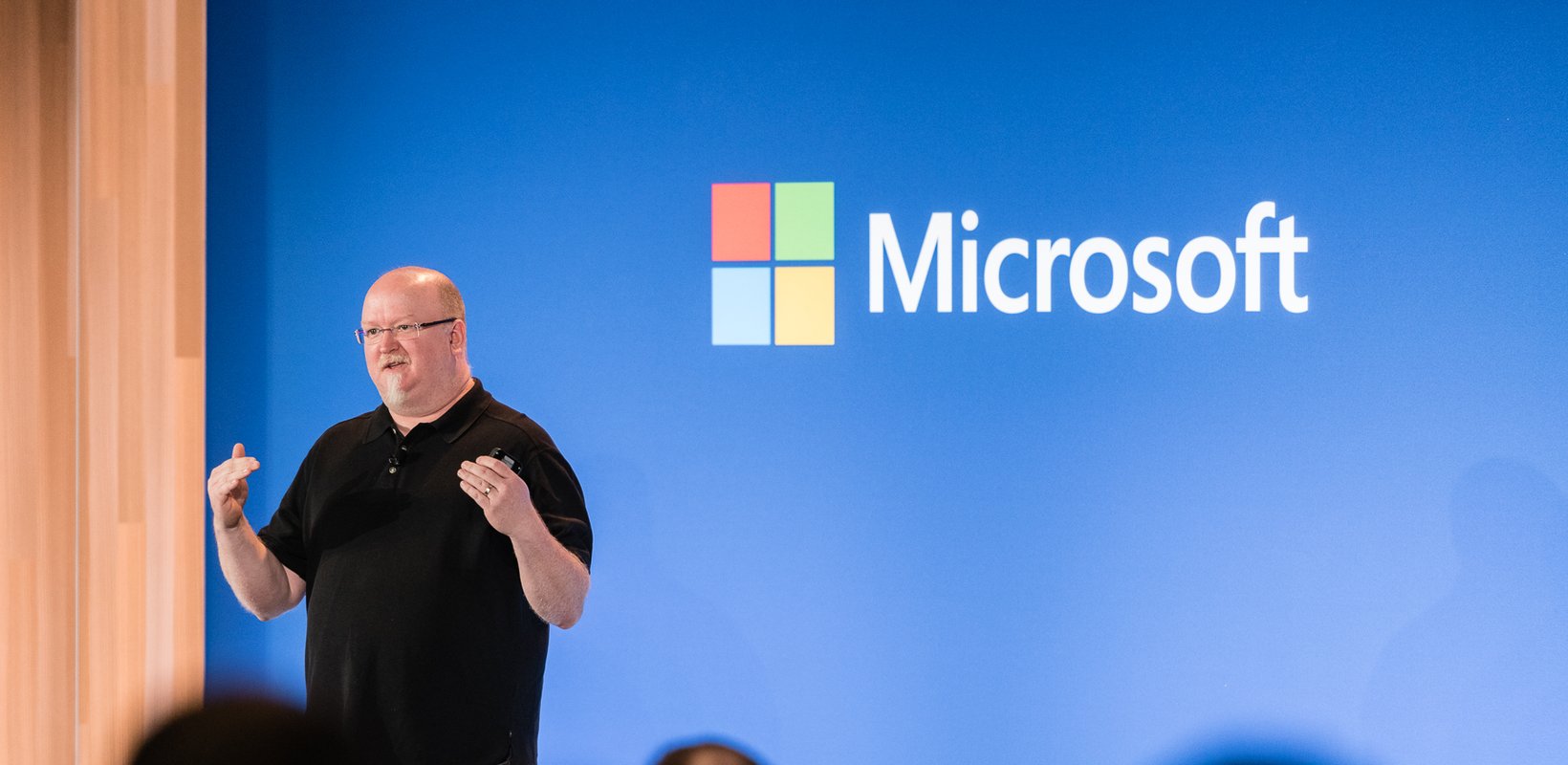 Microsoft CTO, Kevin Scott, addresses an audience regarding the importance of Artificial Intelligence (AI) learning with Microsoft's logo in the background