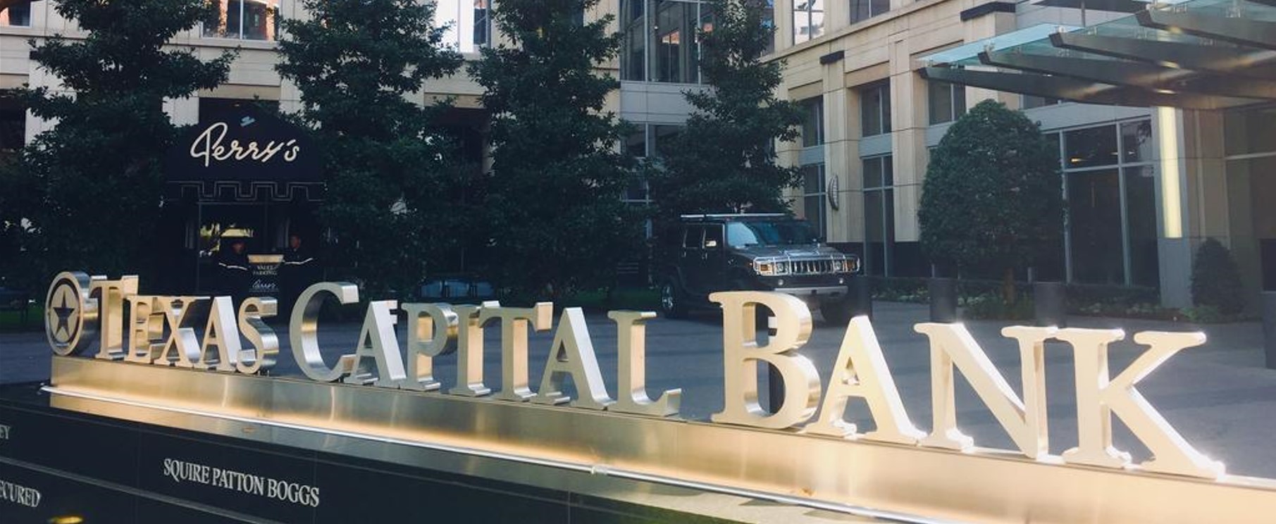In front of the bank building, a Texas Capital Bank sign is shown alongside a few trees and a black car.