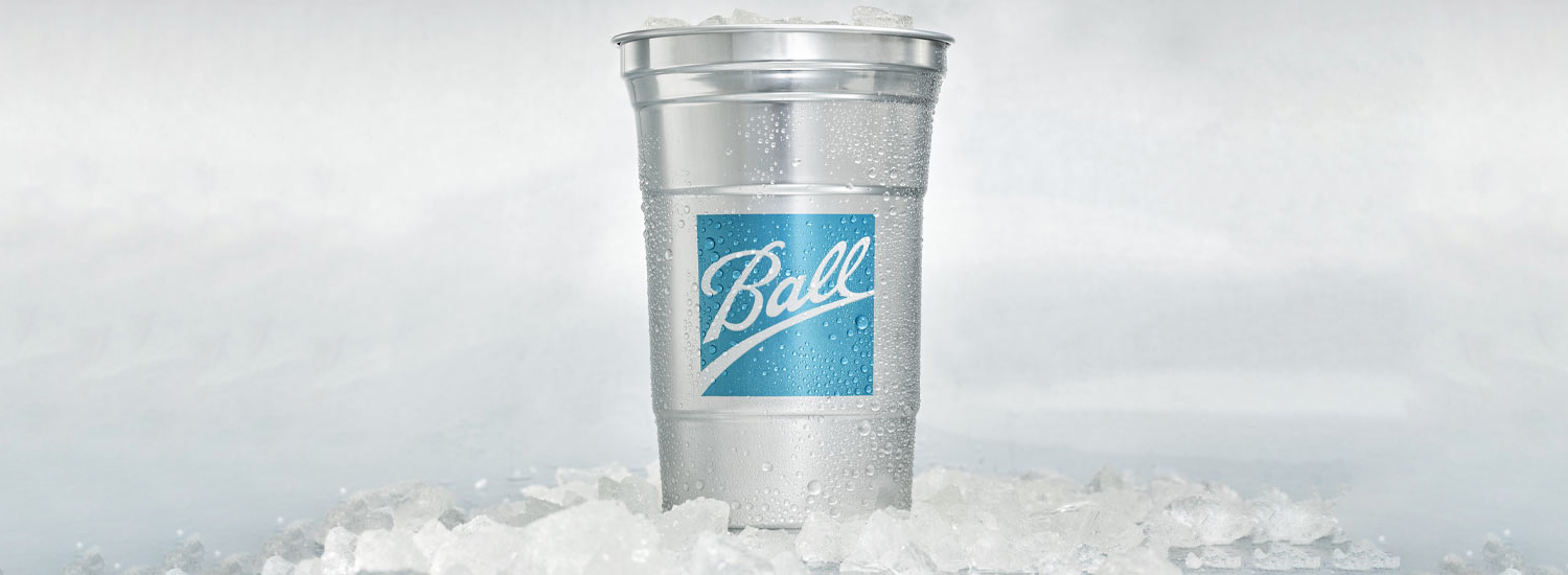 A silver-colored glass with the Ball emblem is set atop ice cubes and filled with more ice cubes.