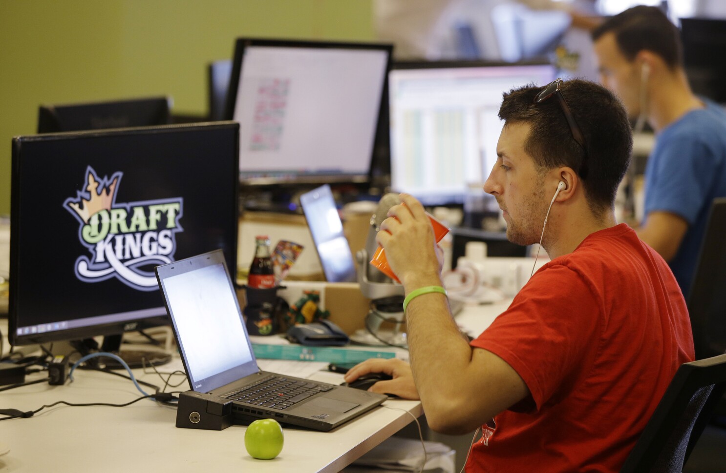 An Employee at DraftKings sips from a plastic cup while working with other colleagues and computer systems in the background