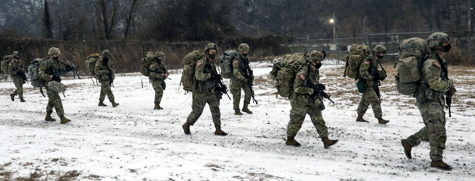 A group of armed soldiers - wearing armed suit and weapons - walking in the snow.