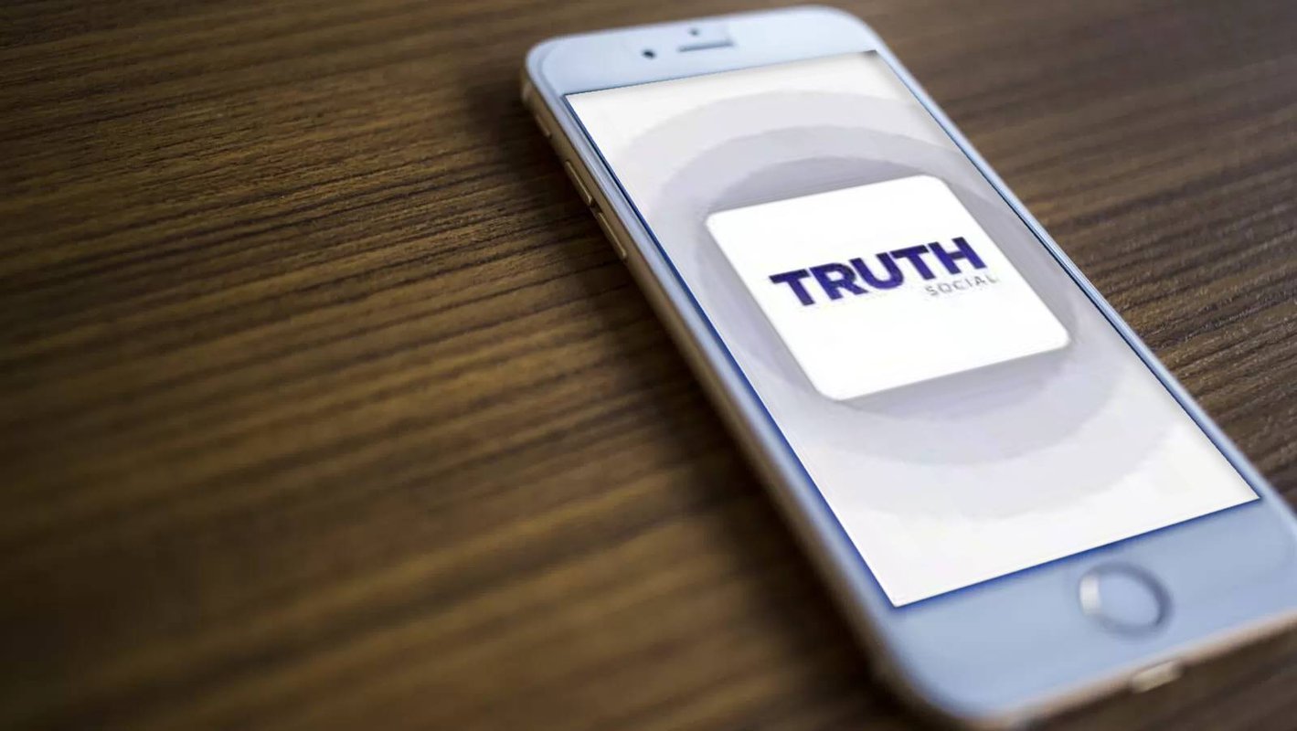 The logo of the Truth app is displayed on a mobile phone that is lying on a table.